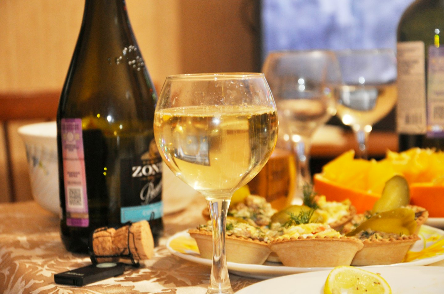 Glass of sparkling wine and Prosecco bottle with snacks on a table.