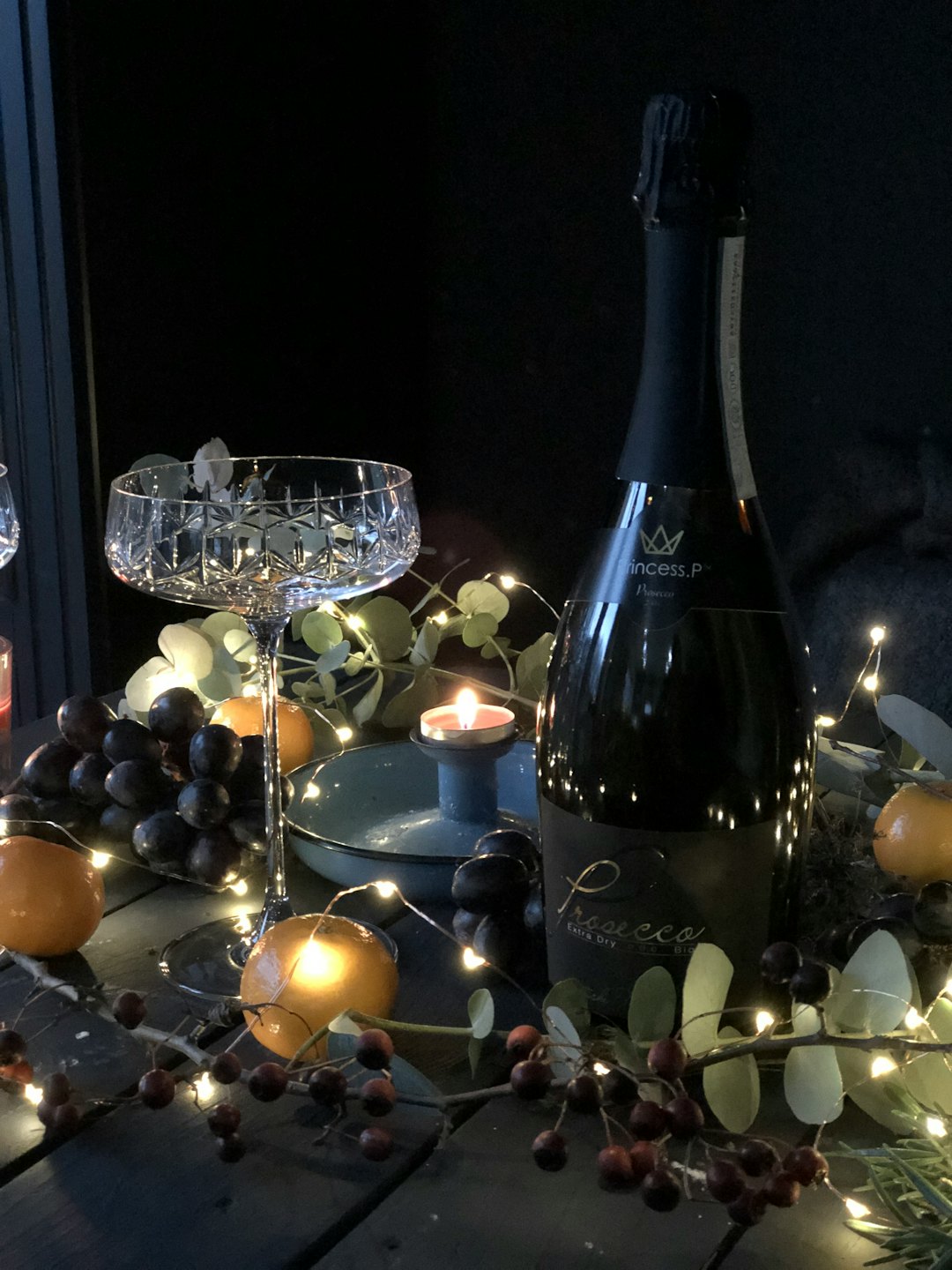 Bottle of Prosecco and coupe glass with fruit and candles.